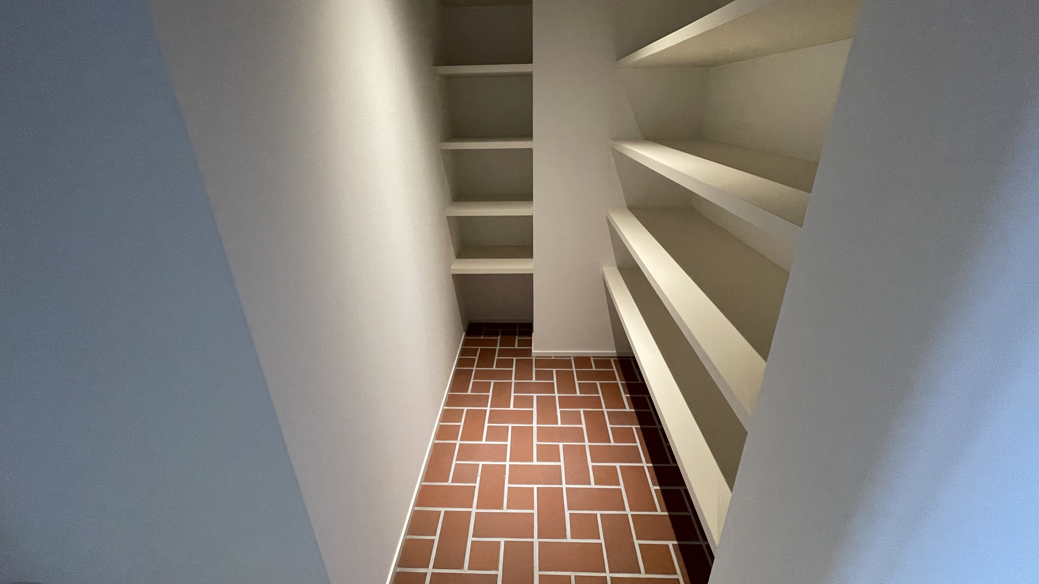 Next to entrance, view of the corridor and the shoes space. Brick flooring style for the entrance and spot lights. Shelves for the shoes storage.